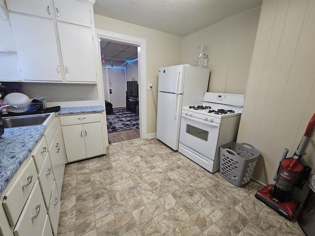 kitchen featuring white appliances, light countertops, a paneled ceiling, white cabinetry, and a sink