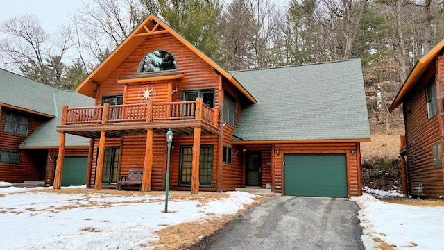 cabin featuring a shingled roof, driveway, a balcony, and an attached garage