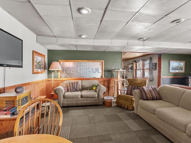 living area featuring a paneled ceiling, wooden walls, carpet flooring, and wainscoting