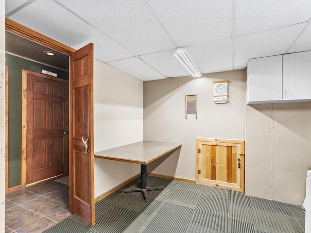 basement with a paneled ceiling and baseboards