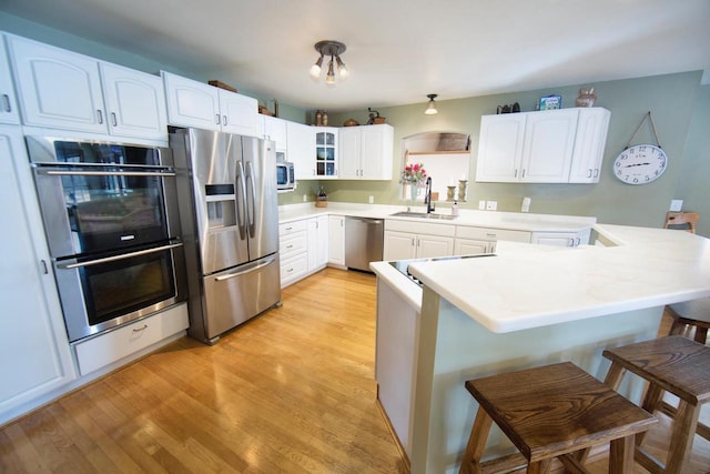 kitchen with a breakfast bar, stainless steel appliances, glass insert cabinets, white cabinetry, and a peninsula