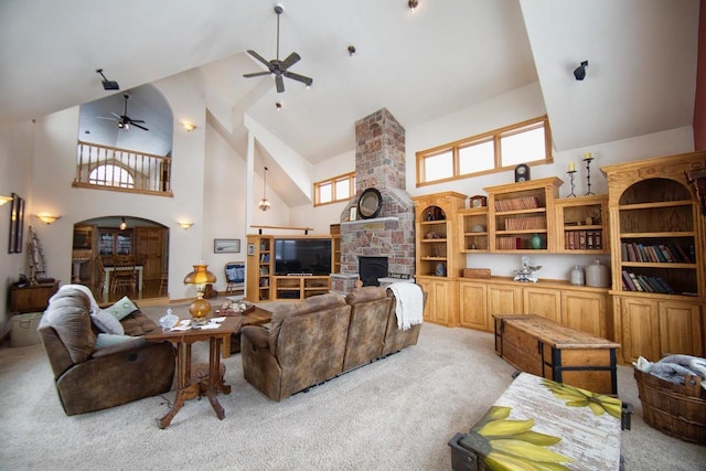 living area with light carpet, arched walkways, a ceiling fan, a stone fireplace, and high vaulted ceiling