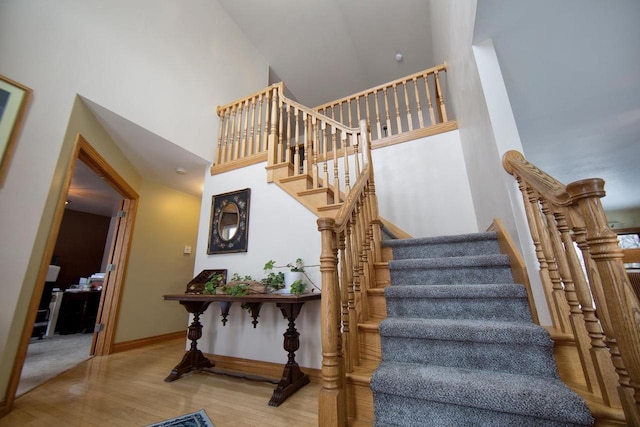 stairs featuring a high ceiling, baseboards, and wood finished floors