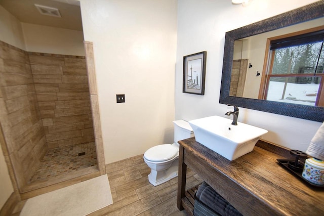 full bath featuring toilet, wood finish floors, a sink, visible vents, and walk in shower