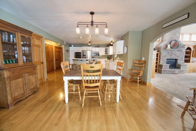 dining area featuring arched walkways, light wood-type flooring, and a stone fireplace