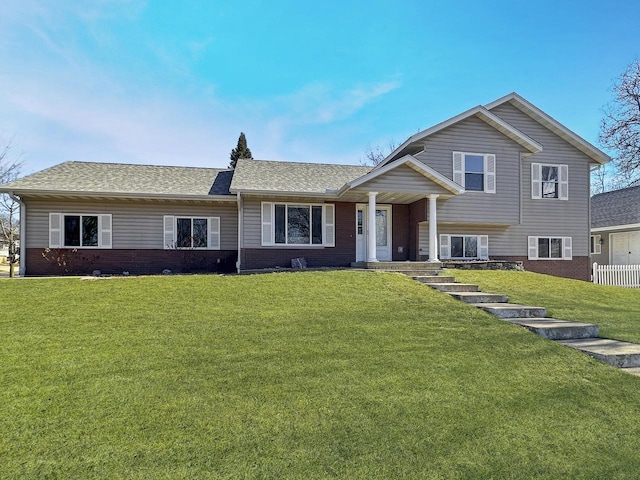 split level home with a front lawn, a shingled roof, and brick siding