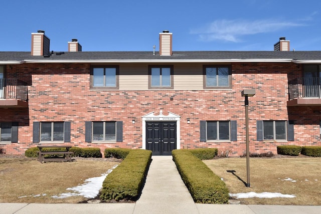 view of front facade with brick siding, a front lawn, and a chimney