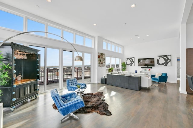 living room featuring recessed lighting, a towering ceiling, baseboards, and wood finished floors