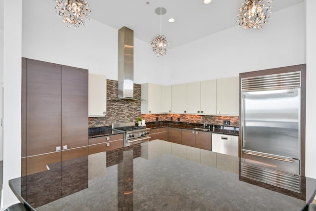 kitchen featuring premium appliances, wall chimney exhaust hood, an inviting chandelier, a high ceiling, and a sink