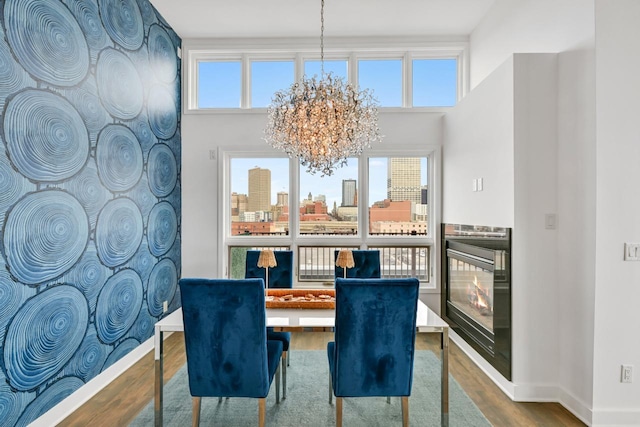 dining room with a city view, a notable chandelier, wood finished floors, a warm lit fireplace, and baseboards