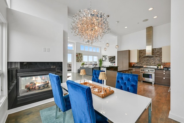 dining room with dark wood-style flooring, a high ceiling, a multi sided fireplace, and an inviting chandelier