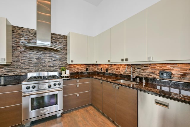 kitchen with a sink, wall chimney range hood, high end range, decorative backsplash, and dark stone countertops