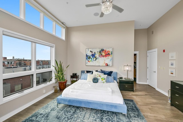 bedroom featuring ceiling fan, wood finished floors, a towering ceiling, and baseboards