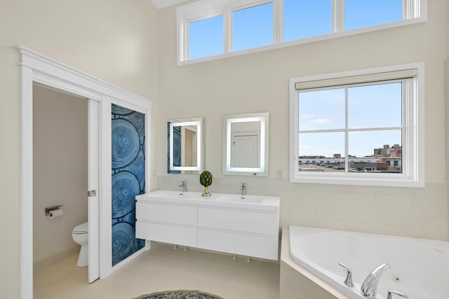 bathroom featuring double vanity, toilet, a jetted tub, tile patterned flooring, and a sink