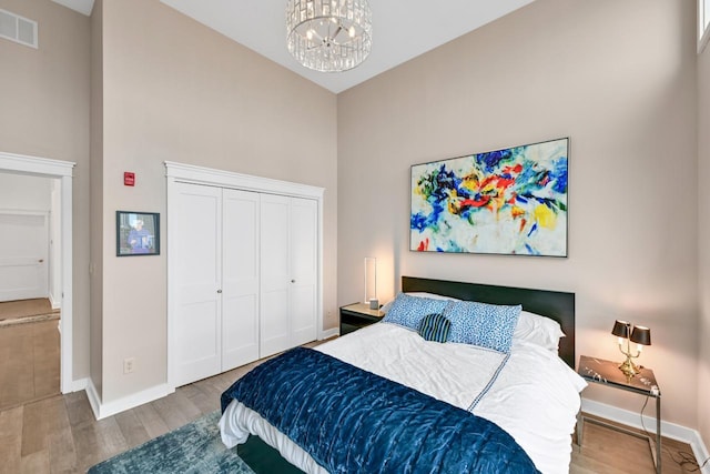 bedroom with high vaulted ceiling, a notable chandelier, wood finished floors, visible vents, and baseboards