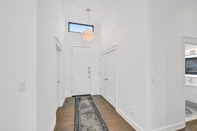 foyer entrance with dark wood-style floors, a notable chandelier, a towering ceiling, and baseboards