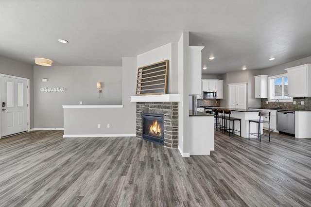 unfurnished living room featuring a stone fireplace, recessed lighting, wood finished floors, and baseboards