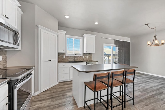 kitchen with dark wood finished floors, stainless steel appliances, dark countertops, white cabinets, and a sink