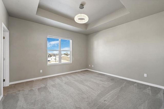 carpeted spare room featuring baseboards and a tray ceiling