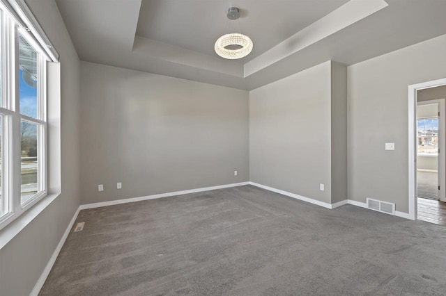 carpeted empty room featuring baseboards, visible vents, and a raised ceiling