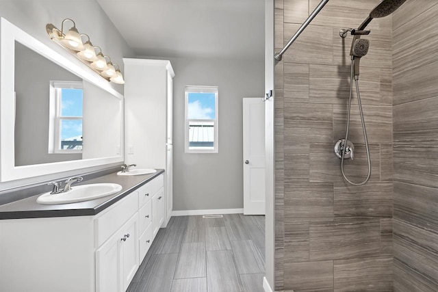 bathroom featuring double vanity, baseboards, a sink, and tiled shower