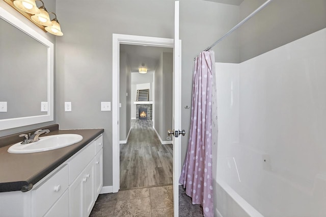 bathroom featuring a lit fireplace, baseboards, shower / bathtub combination with curtain, and vanity