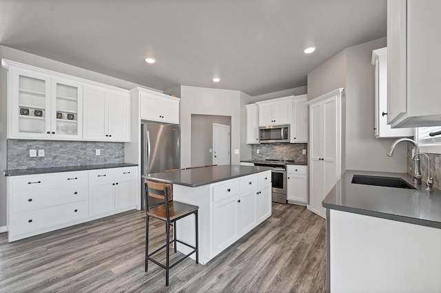 kitchen featuring white cabinets, dark countertops, a kitchen island, appliances with stainless steel finishes, and a sink