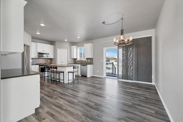 kitchen with a center island, a breakfast bar, stainless steel appliances, dark countertops, and white cabinetry