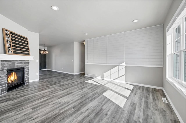 unfurnished living room featuring a fireplace, wood finished floors, visible vents, baseboards, and an inviting chandelier