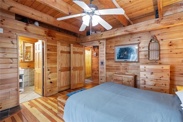 bedroom featuring light wood finished floors, wood ceiling, connected bathroom, wood walls, and beamed ceiling