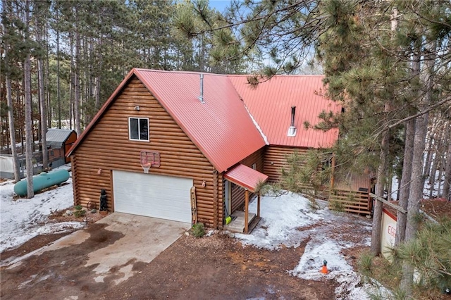 snow covered property with metal roof, log exterior, driveway, and a garage