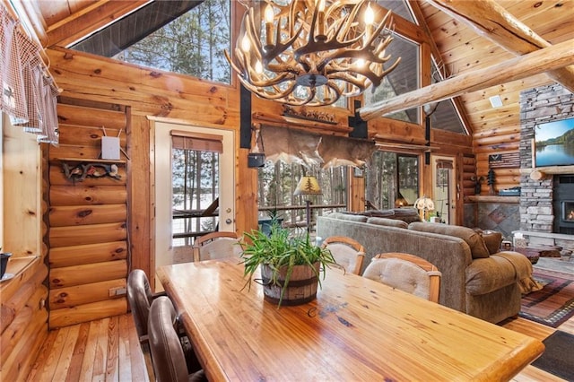 dining room featuring a stone fireplace, hardwood / wood-style flooring, a notable chandelier, wood ceiling, and beam ceiling