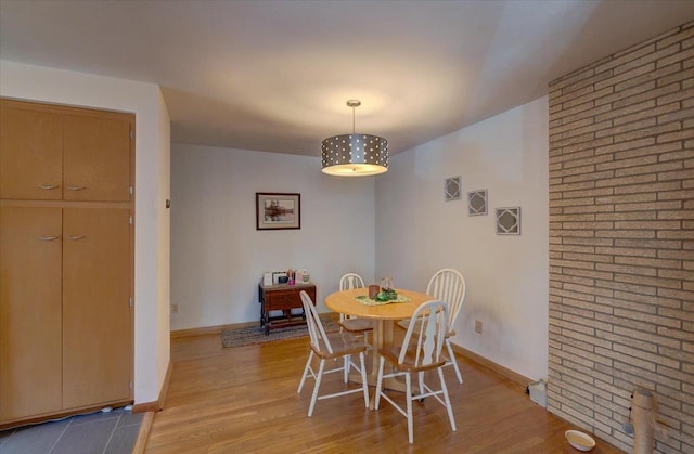 dining room featuring brick wall, baseboards, and light wood-style floors