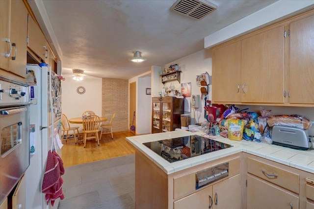 kitchen featuring visible vents, freestanding refrigerator, tile countertops, a peninsula, and black electric stovetop