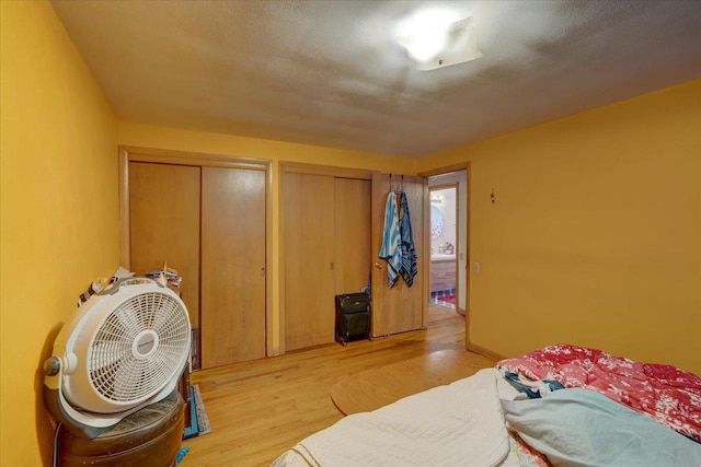 bedroom featuring light wood-style floors, multiple closets, and a textured ceiling