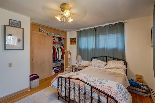 bedroom with wood finished floors, a closet, baseboard heating, and ceiling fan