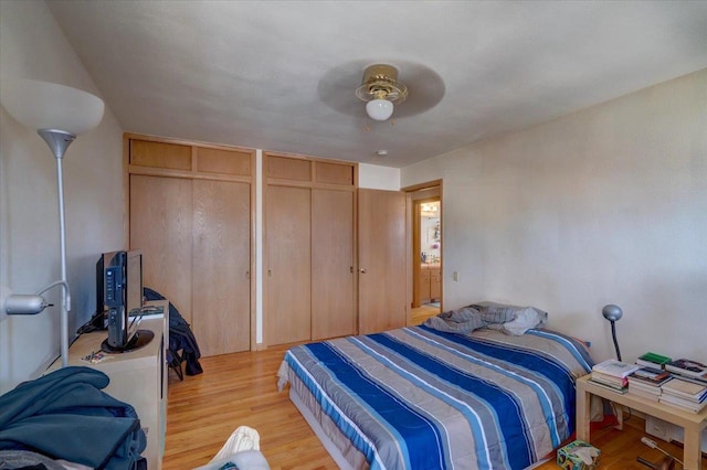 bedroom featuring light wood-type flooring, two closets, and ceiling fan