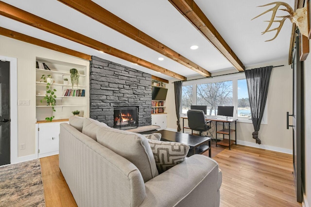 living area with beam ceiling, baseboards, light wood-style floors, and a stone fireplace