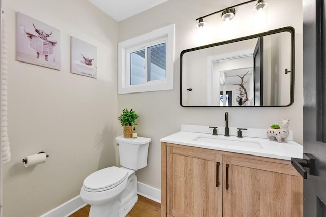 half bath featuring baseboards, toilet, and vanity