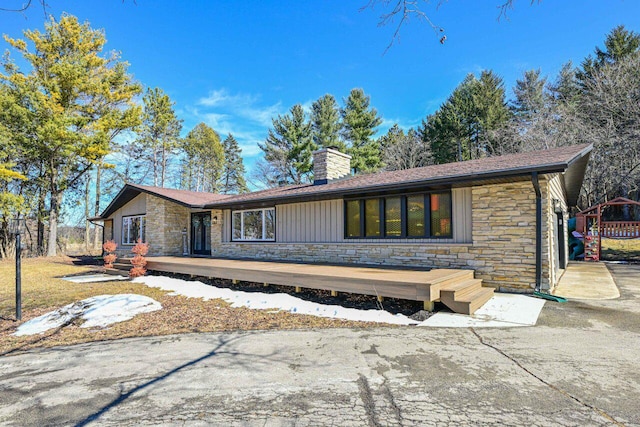 mid-century modern home with stone siding, board and batten siding, and a chimney