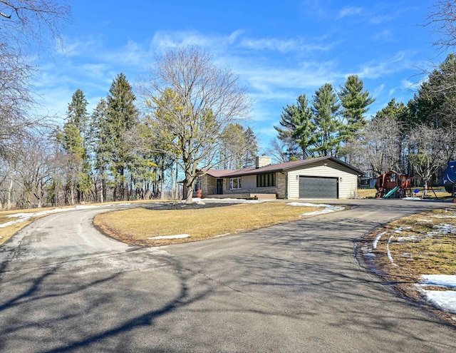 view of front of home with playground community, a chimney, a front lawn, a garage, and aphalt driveway