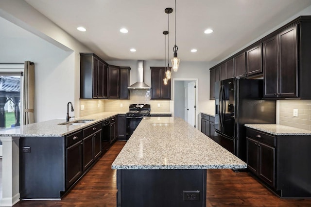 kitchen featuring wall chimney exhaust hood, dark wood-style flooring, hanging light fixtures, black appliances, and a sink