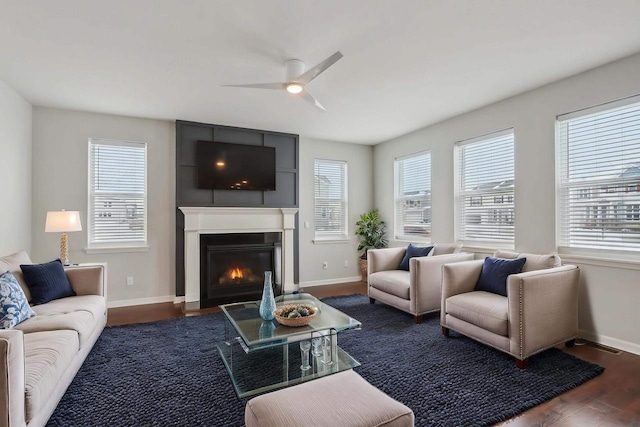 living area featuring ceiling fan, dark wood-type flooring, a glass covered fireplace, and baseboards