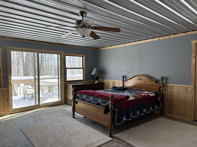 bedroom featuring access to outside, wood walls, wainscoting, and a ceiling fan