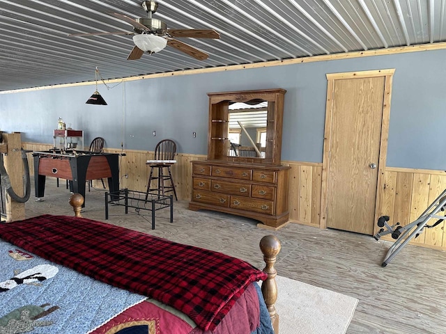 bedroom featuring a wainscoted wall, wooden walls, and light wood finished floors