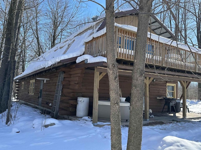 view of snowy exterior featuring a deck, log siding, and a garage