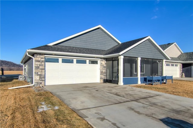 view of front facade with concrete driveway, a front yard, a sunroom, a garage, and stone siding