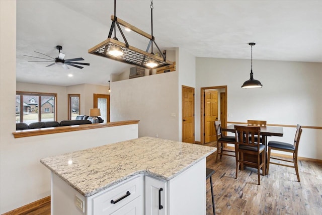 kitchen featuring light wood-style flooring, a kitchen island, light stone counters, vaulted ceiling, and white cabinetry