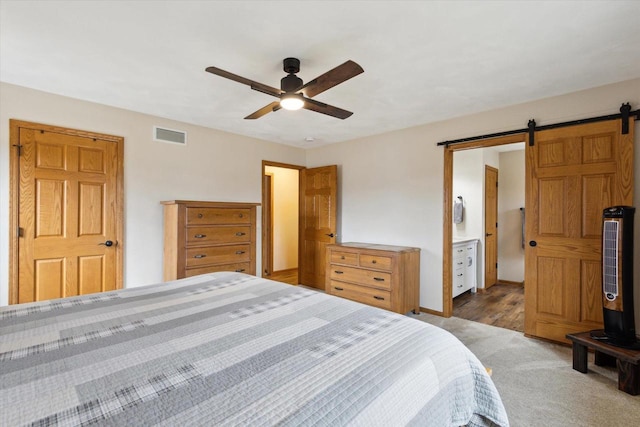 carpeted bedroom with ensuite bathroom, a barn door, visible vents, baseboards, and a ceiling fan