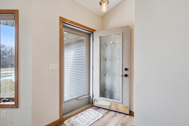 doorway featuring baseboards, vaulted ceiling, and wood finished floors